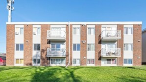 A multi-story apartment building with balconies, a clear sky, and a well-maintained lawn.