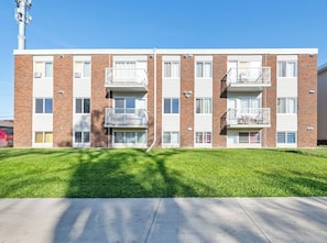 A multi-story apartment building with balconies, a clear sky, and a well-maintained lawn.
