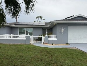 Ein Wohnhaus mit Garage, einem weißen Zaun und einer Palme im Vordergrund.
