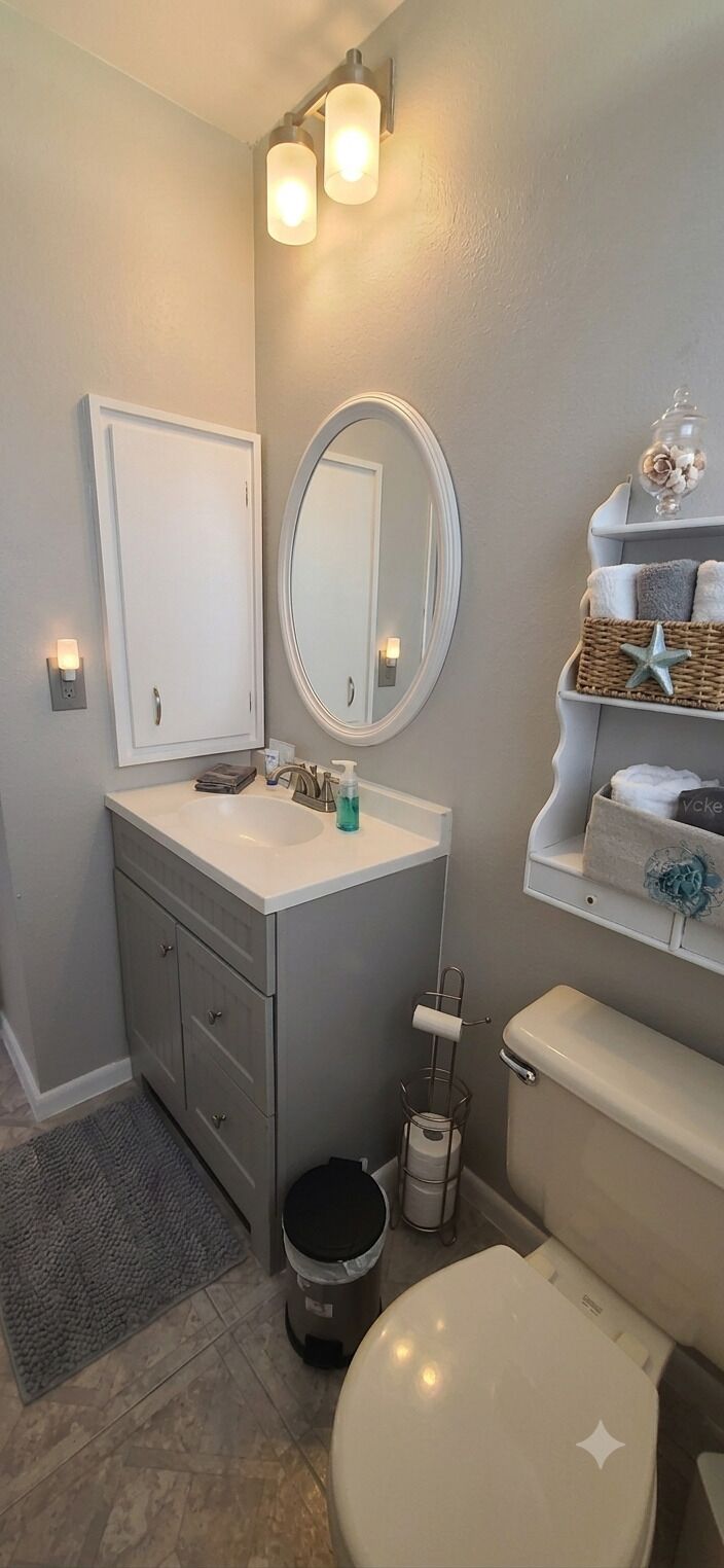 Une salle de bain comprenant des toilettes, un lavabo, un meuble-lavabo, un miroir et un espace pour ranger les serviettes.