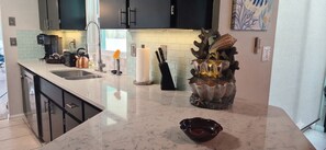 A modern kitchen with a marble countertop, a coffee maker, a kettle, and a decorative shell sculpture. - 3 Bedroom Pet-friendly Home with Pool (Port Charlotte)