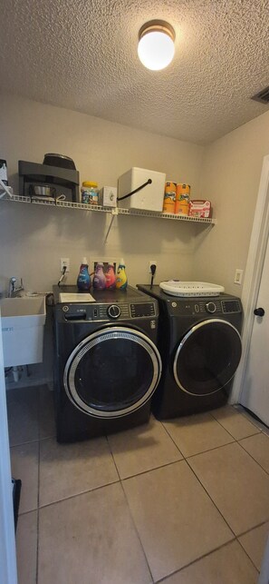 Una sala de bugaderia amb dues rentadores de càrrega frontal, un rentapeus i prestatges amb productes de neteja.
