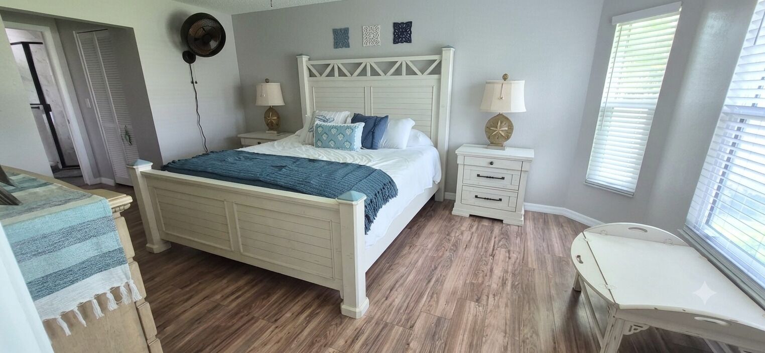 A bedroom with a bed, bedside tables, a fan, and a window with blinds.