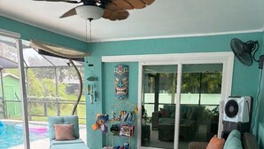 Une pièce meublée de mobilier en osier, dotée d’un ventilateur de plafond et offrant une vue sur une piscine.