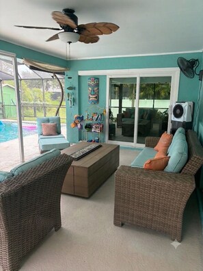 Ein Zimmer mit Korbmöbeln, einem Deckenventilator und Blick auf einen Swimmingpool.