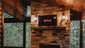 Une pièce chaleureuse avec une cheminée en pierre, des fauteuils en osier et un écran de télévision affichant le logo « NETFLIX ».