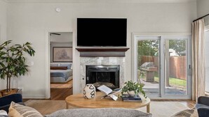 A living room with a fireplace, a television, and a sliding glass door to the outside. - Casa Joya @ Jenks Spain Ranch/Five Oaks (Jenks)