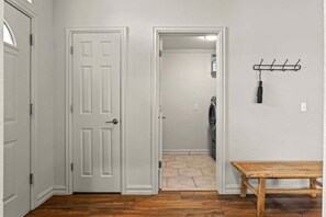 A hallway with a wooden bench, a coat rack, and a door leading to a laundry room. - Casa Joya @ Jenks Spain Ranch/Five Oaks (Jenks)
