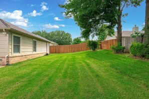 A residential backyard with a wooden fence, a lawn, and a house. - Casa Joya @ Jenks Spain Ranch/Five Oaks (Jenks)