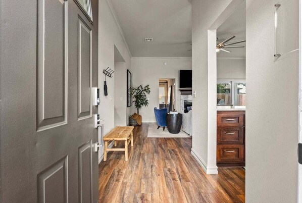 A hallway with wooden flooring, a bench, a potted plant, and a kitchen area with cabinets and a TV. - Casa Joya @ Jenks Spain Ranch/Five Oaks (Jenks)