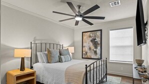 A bedroom with a bed, a ceiling fan, a nightstand, a lamp, a painting, a window, and a TV. - Casa Joya @ Jenks Spain Ranch/Five Oaks (Jenks)
