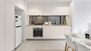 A modern kitchen with white cabinetry, a built-in oven, a gas stove, and a dining area with a table and chairs. - Sleek 1BR Apartment | Home of Mortlake Ferry (Mortlake)