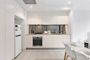 A modern kitchen with white cabinetry, a built-in oven, a gas stove, and a dining area with a table and chairs. - Sleek 1BR Apartment | Home of Mortlake Ferry (Mortlake)