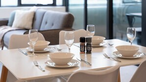 A dining table set with white plates, bowls, and cutlery, with salt and pepper shakers and glasses of water. - Sleek 1BR Apartment | Home of Mortlake Ferry (Mortlake)
