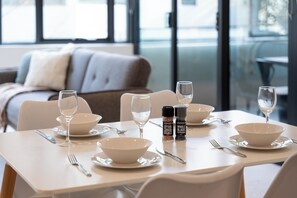 A dining table set with white plates, bowls, and cutlery, with salt and pepper shakers and glasses of water. - Sleek 1BR Apartment | Home of Mortlake Ferry (Mortlake)