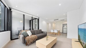 A modern living room with a sofa, coffee table, and TV. - Sleek 1BR Apartment | Home of Mortlake Ferry (Mortlake)