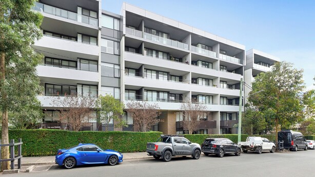 A multi-story residential building with balconies, parked cars, and a clear sky. - Sleek 1BR Apartment | Home of Mortlake Ferry (Mortlake)