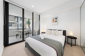 A modern bedroom with a large bed, a view of the outside balcony, and a small table with chairs. - Sleek 1BR Apartment | Home of Mortlake Ferry (Mortlake)