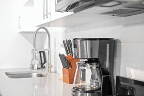 A kitchen with a coffee maker, knife set, and a glass carafe on the counter. - Boutique-Style Studio Unit (Edmonton)