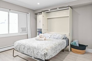A bedroom with a bed, a window, a wardrobe, and a bedside table. - Boutique-Style Studio Unit (Edmonton)