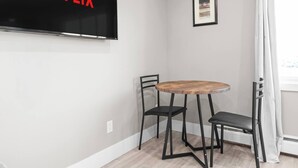 Ett rum med en tv-skärm som visar ordet ”NETFLIX” med röda bokstäver, ett runt träbord med två svarta stolar och en inramad tavla på väggen.