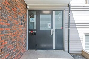 A black door with a keypad and a card reader, a window with a security camera, and a brick wall. - Boutique-Style Studio Unit (Edmonton)