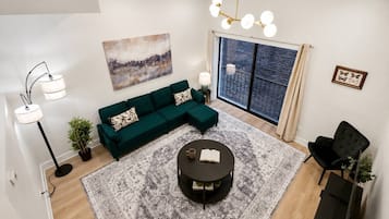 Ein modernes Wohnzimmer mit einem grünen Sofa, einem runden Couchtisch, einer Stehlampe und einem großen Fenster mit Blick.