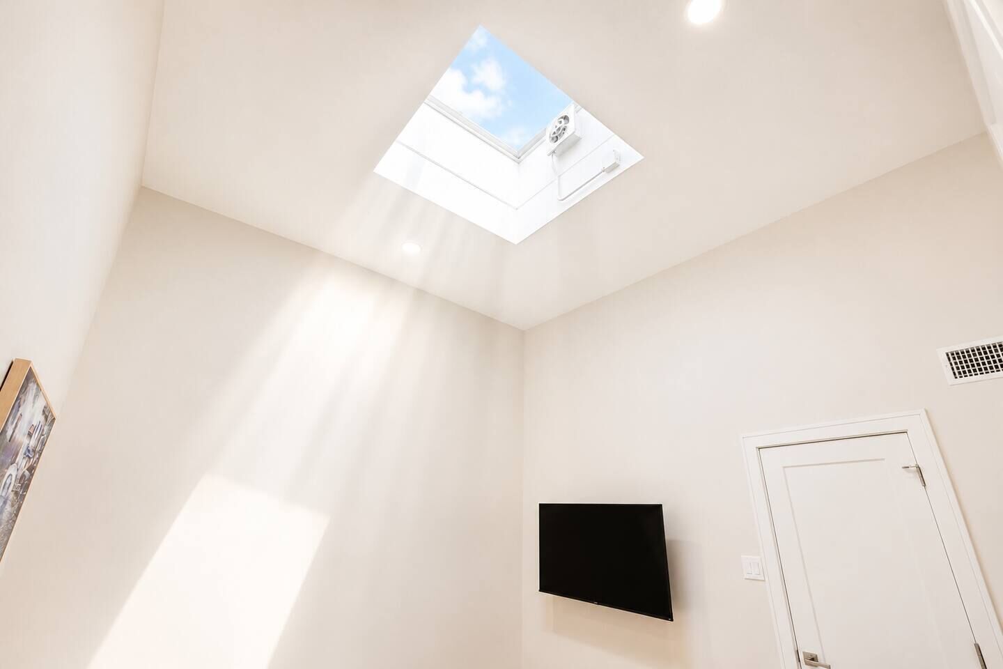 Quarto com claraboia, televisão montada e uma porta.