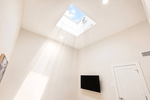 Quarto com claraboia, televisão montada e uma porta.
