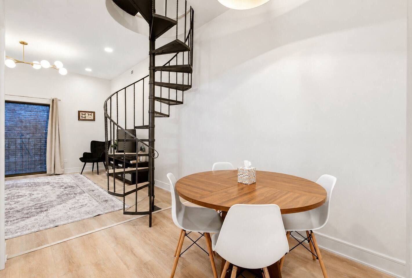 Um interior moderno com uma escada em espiral, uma mesa de jantar redonda de madeira e cadeiras brancas.