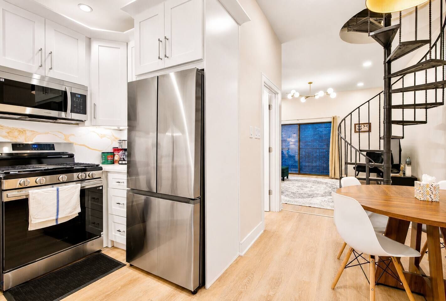 Una cocina moderna con electrodomésticos de acero inoxidable, un comedor con mesa de madera y una escalera de caracol.