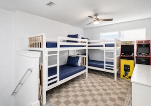 A room with bunk beds, a ceiling fan, arcade games, and a checkered floor. - Destin Dreamin': 7 King Suites, Heated Pool, Golf Cart & Arcade Bunk Room (Miramar Beach)