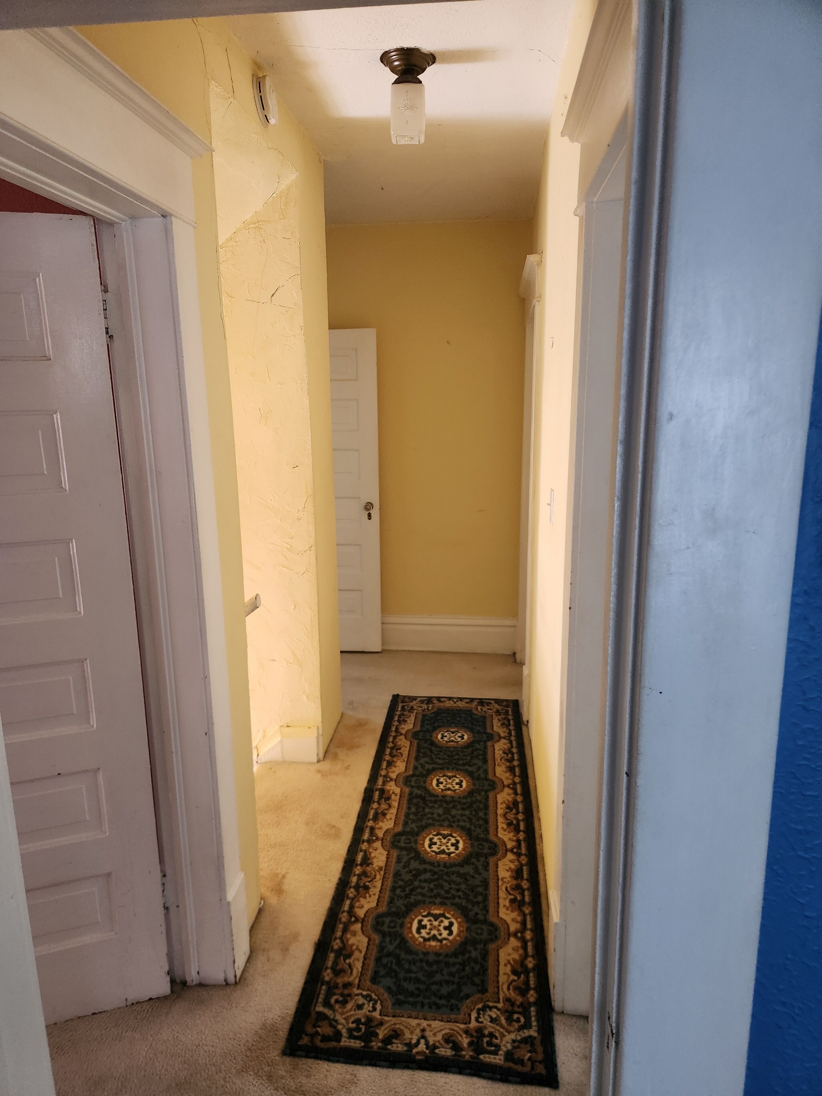 A hallway with a carpet, a ceiling fan, and a door.