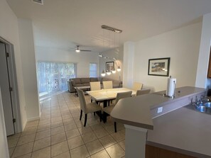 Eine moderne Küche mit Essbereich, inklusive einer großen Kochinsel, Deckenventilator und Blick durch das Fenster.