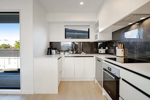 A modern kitchen with white cabinetry, a black countertop, a built-in oven, and a large window.