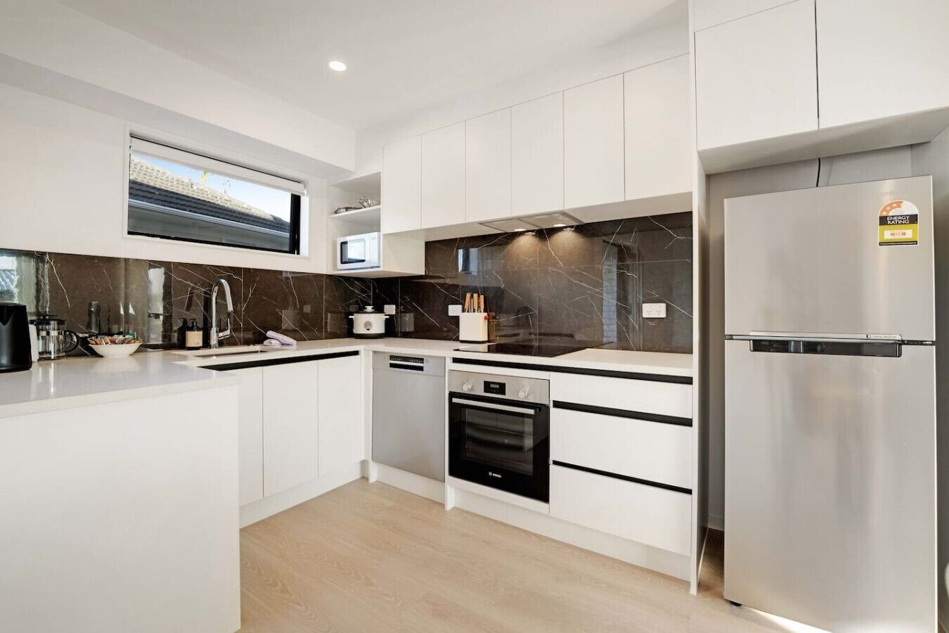 A modern kitchen with white cabinetry, a built-in oven, a microwave, and a stainless steel refrigerator.