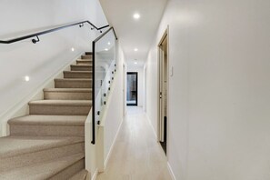 A modern interior with a carpeted staircase, a hallway leading to a door, and recessed lighting.