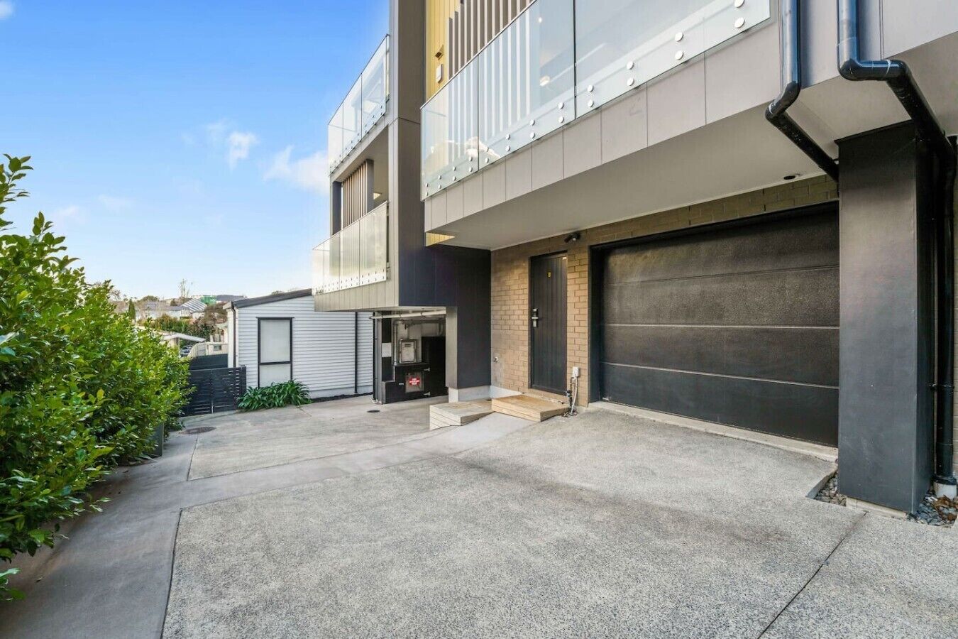 A modern two-story building with a garage, a small entrance, and a concrete driveway.