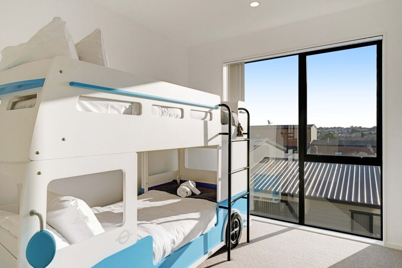 A bunk bed room with a view of a residential area through a large window.