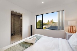 A hotel room with a bed, a window with a view, a bedside table with a lamp, and a shower area.