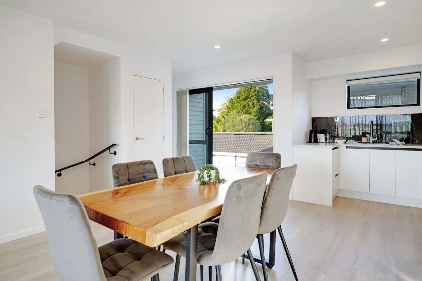 A modern kitchen with a dining area, a large window, and a staircase.