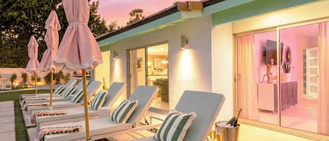 A poolside area with lounge chairs, umbrellas, and a bar area with a bottle of champagne.