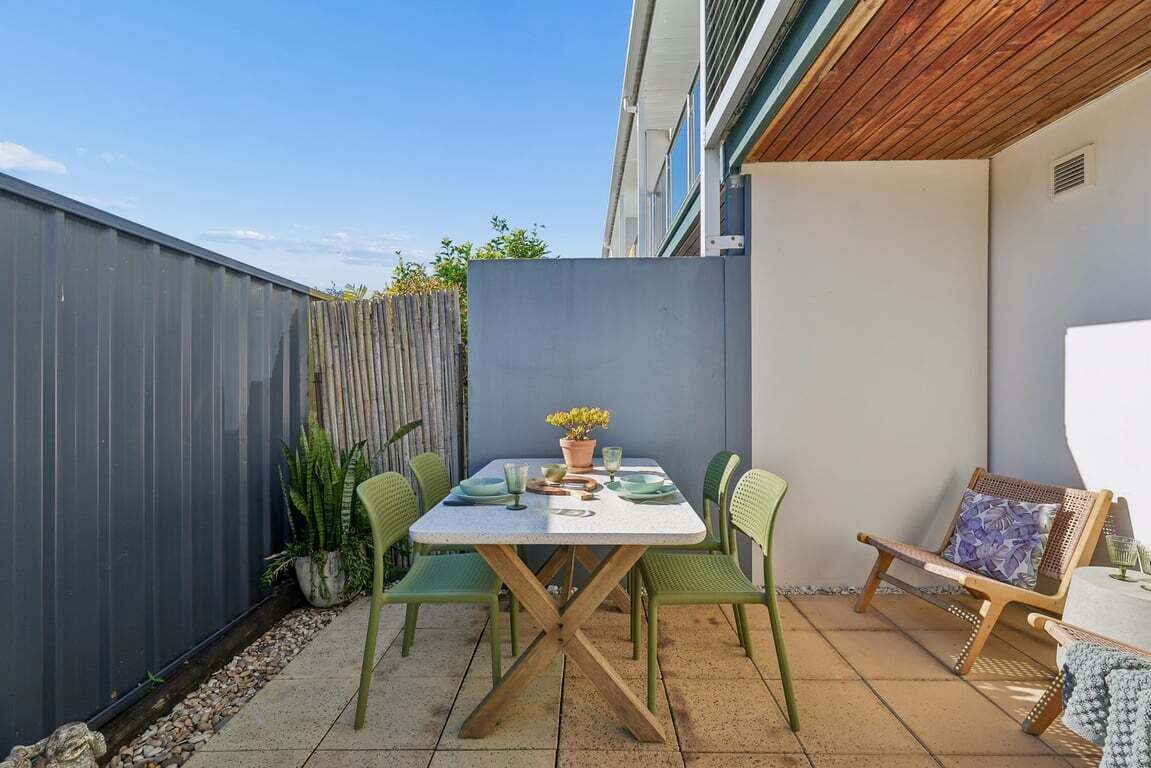 A patio with a table and chairs, a wooden fence, and a potted plant.