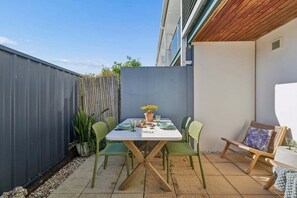 A patio with a table and chairs, a wooden fence, and a potted plant. - Murrays Beach Studio (Sawtell)