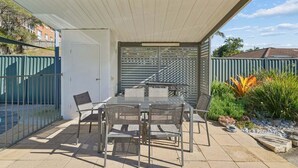 An outdoor patio with a table and chairs, a covered area, and a view of a residential neighborhood. - Murrays Beach Studio (Sawtell)