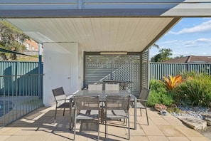 An outdoor patio with a table and chairs, a covered area, and a view of a residential neighborhood. - Murrays Beach Studio (Sawtell)