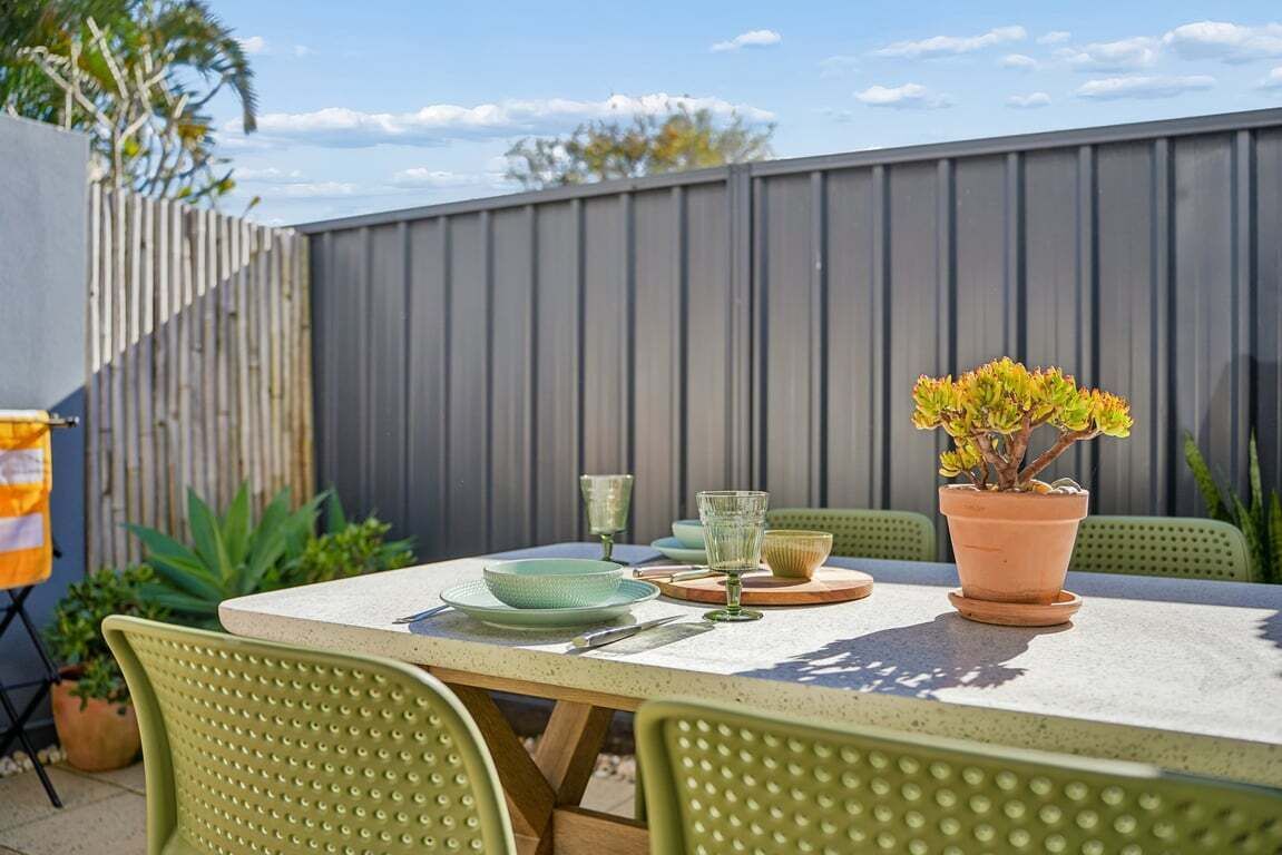 Une terrasse extérieure avec une table dressée pour le repas, entourée de chaises vertes, et une plante en pot posée sur la table.