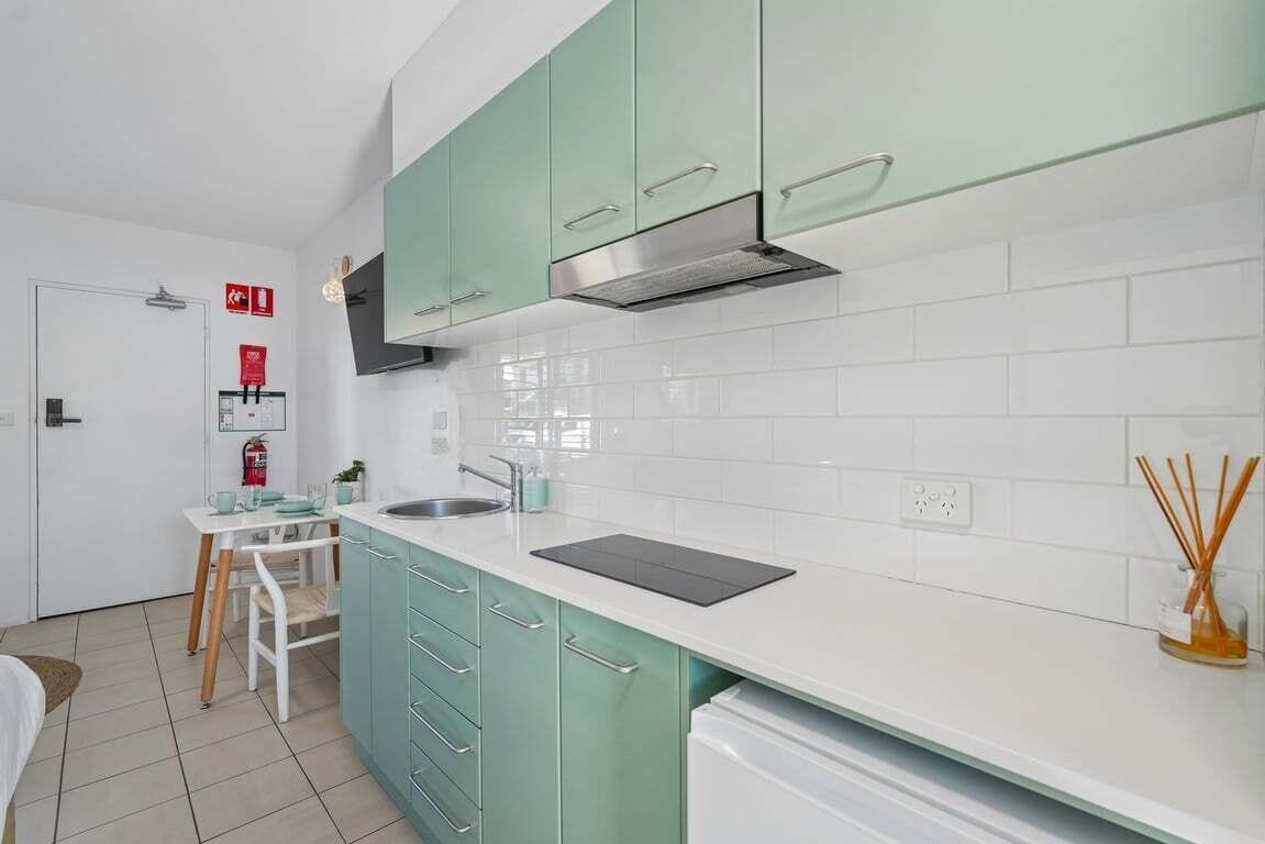 A modern kitchen with teal cabinets, a white countertop, and a stainless steel range hood.