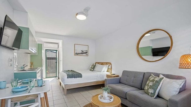 A modern bedroom with a bed, bedside table, and a round mirror. - Murrays Beach Studio (Sawtell)