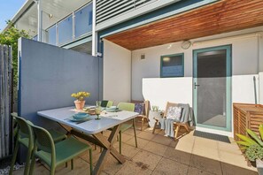 An outdoor patio with a table set for dining, surrounded by chairs and a wooden fence. - Murrays Beach Studio (Sawtell)